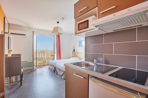 Una habitación de hotel moderna con kitchenette, una cama, un balcón con vistas y un comedor.