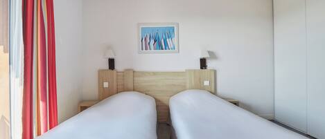 A hotel room with two single beds, a wooden headboard, a painting on the wall, and a window with curtains.