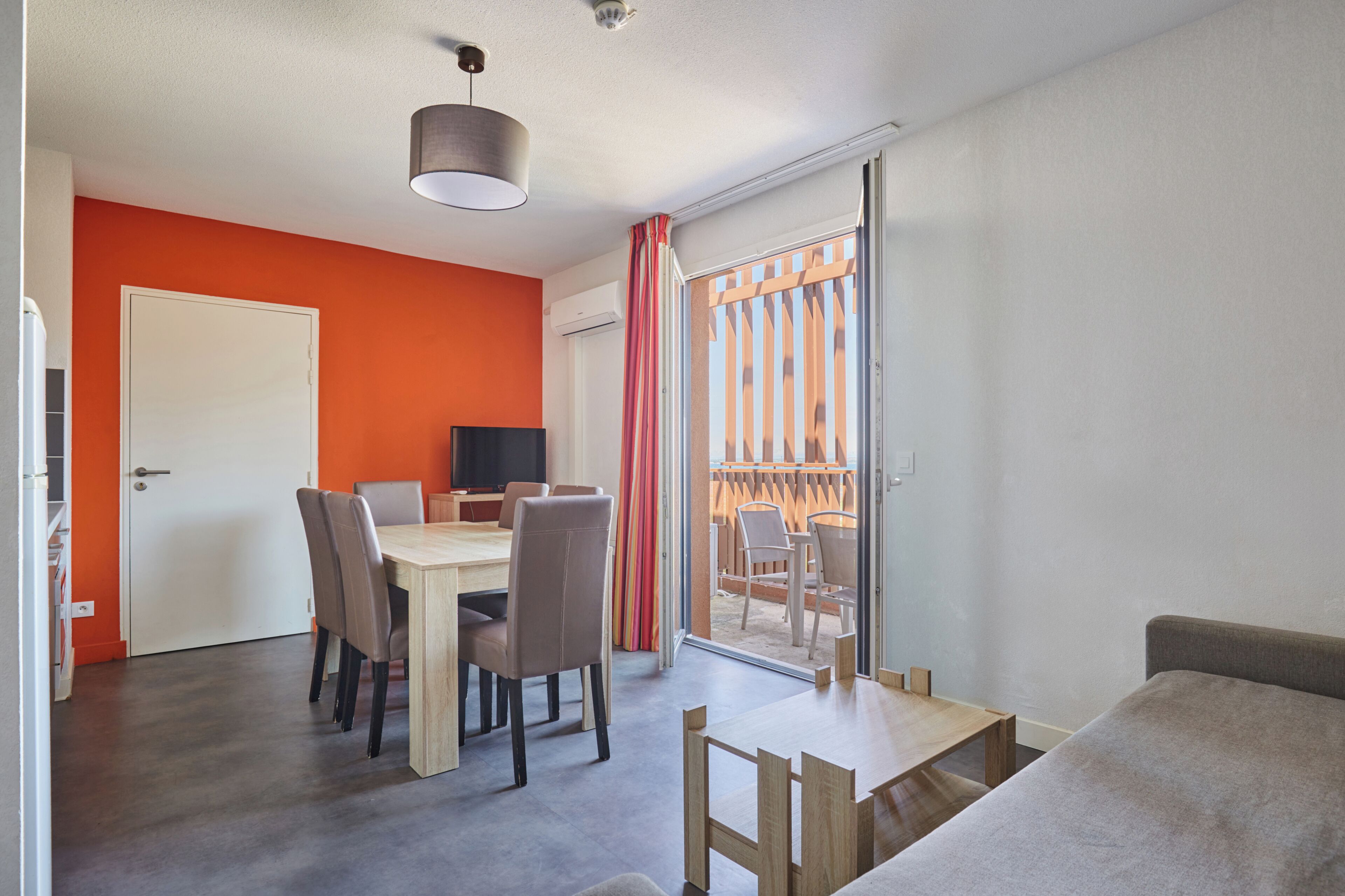 A modern room with a dining table, chairs, a TV, and a sliding glass door leading to an outdoor area.