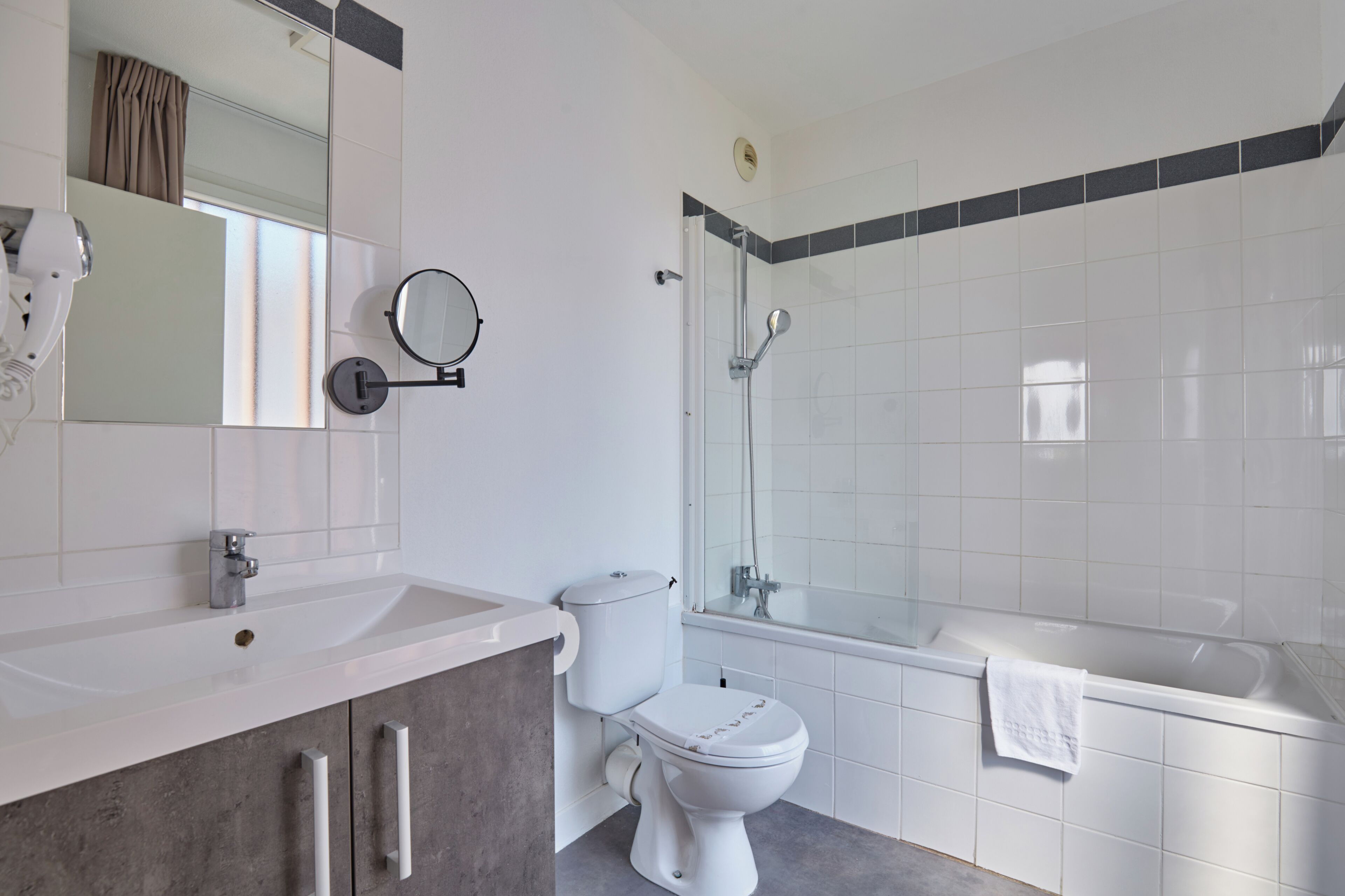 Une salle de bain moderne avec un lavabo, des toilettes et une baignoire blancs, un espace douche et un miroir doté d’un cadre rond.