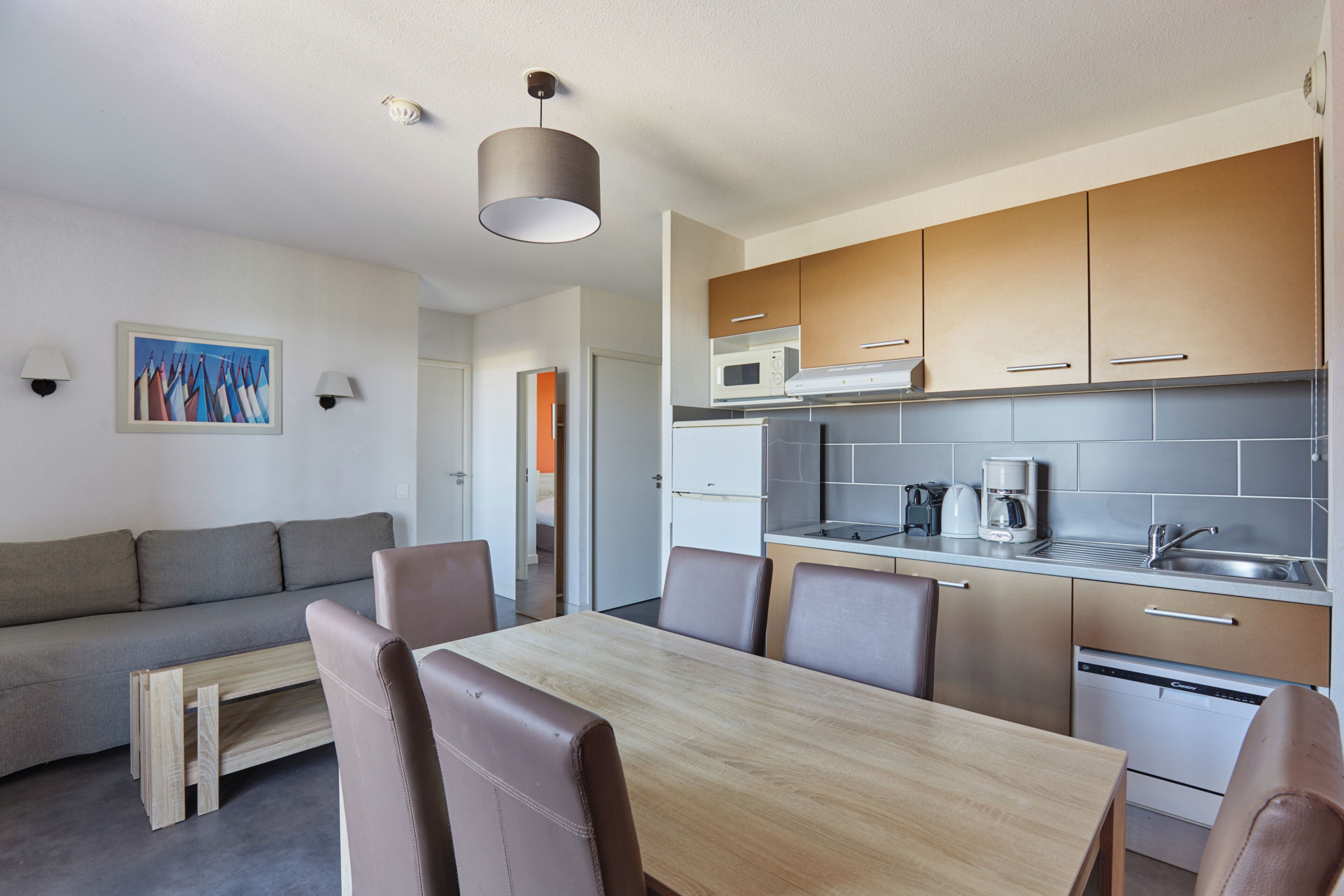 A modern kitchen with a dining area, a sofa, and a painting on the wall.