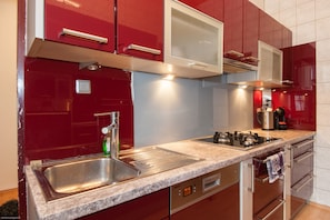 A modern kitchen with red cabinets, stainless steel appliances, and a built-in oven.