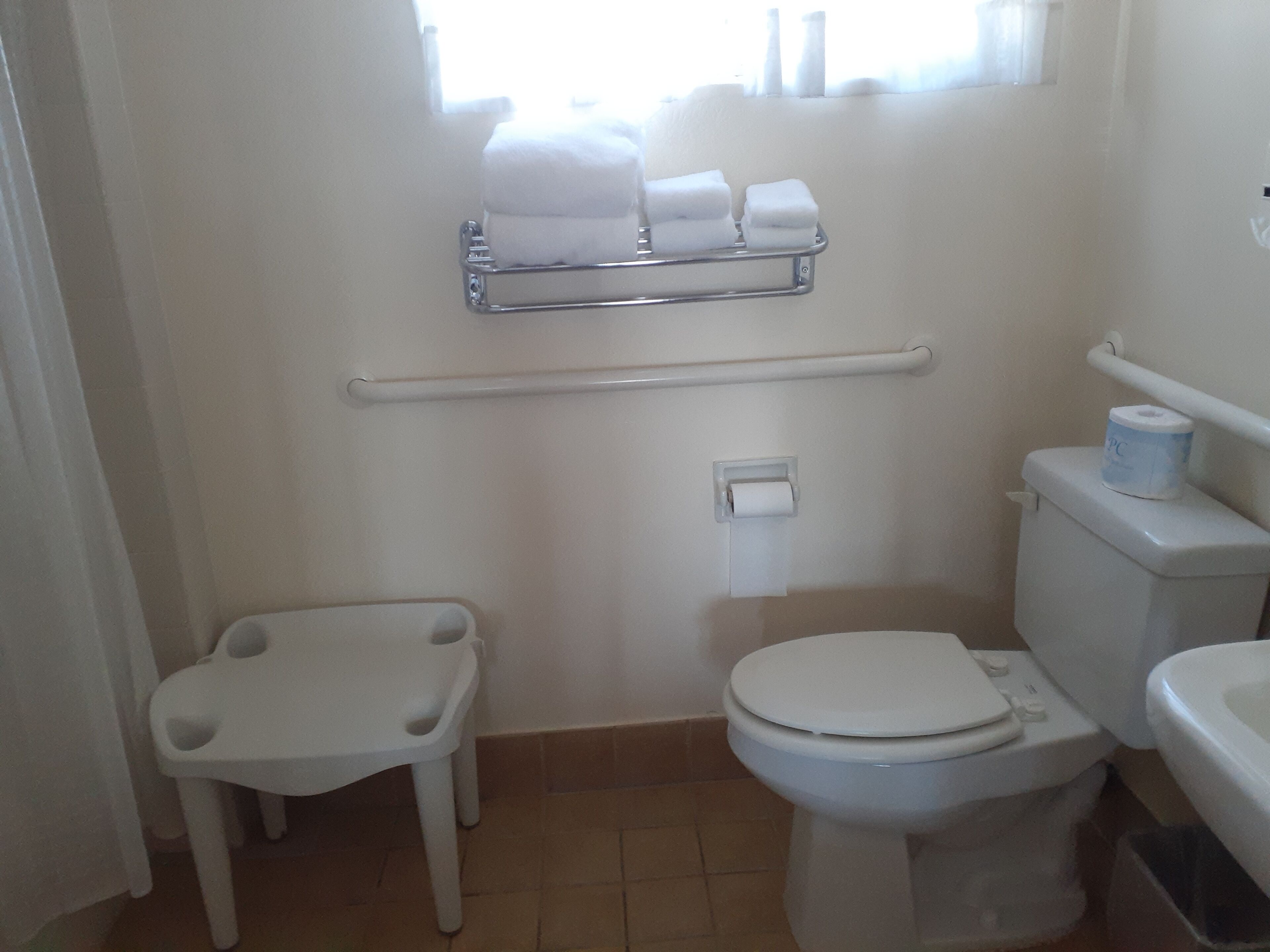 A small, clean bathroom with a toilet, a sink, a shelf with towels, and a roll of toilet paper.