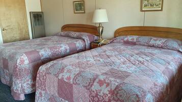 A hotel room with two beds, a bedside lamp, a telephone, and two framed pictures on the wall.