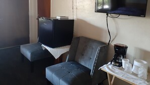 Une pièce de taille modeste, dotée d’un téléviseur fixé au mur, d’une petite table avec des tasses et une machine à café, ainsi que d’un coin salon confortable.