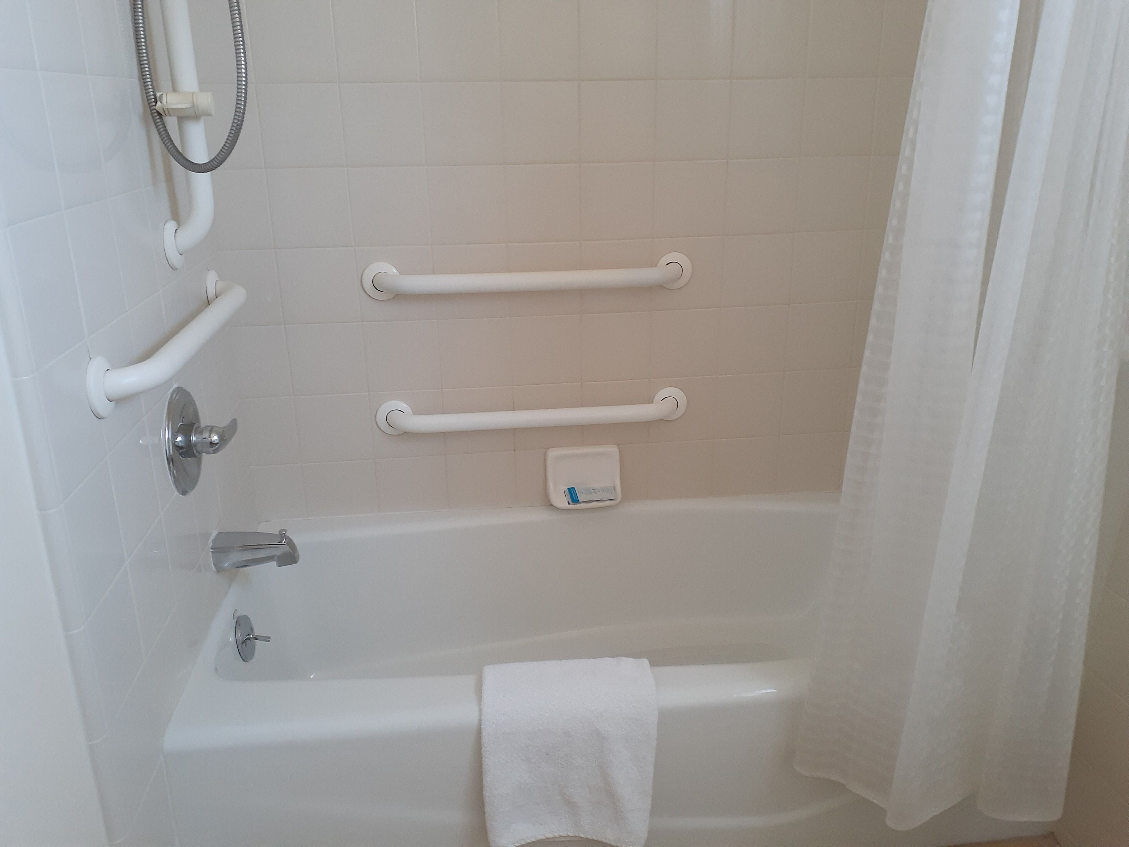 Baño con bañera, barras de apoyo, cabezal de ducha y perchero.
