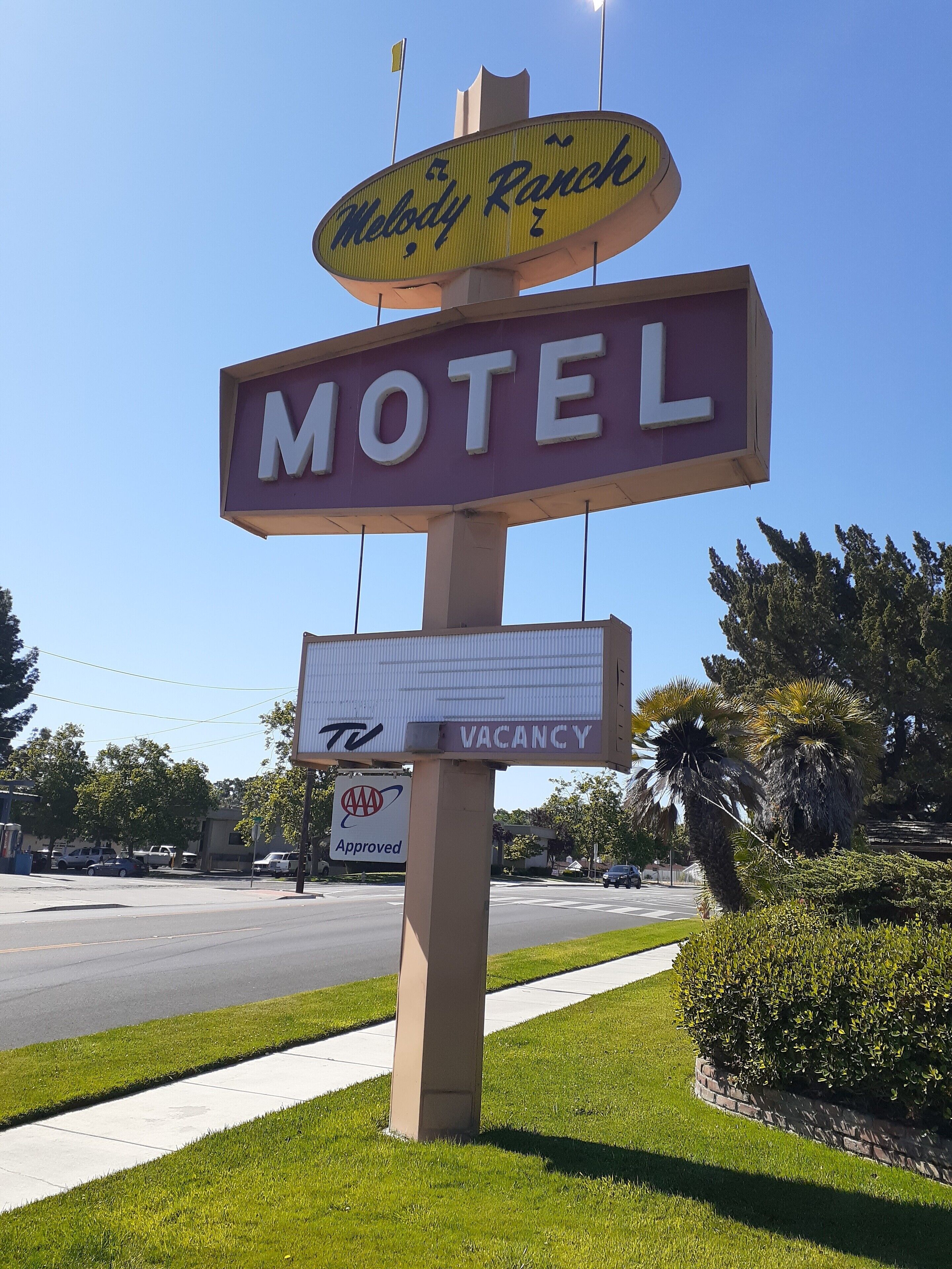 Une enseigne de motel avec l’inscription « Motel », une autre enseigne « Melody Ranch » au-dessus, et une enseigne « TV » et « CHAMBRES LIBRES » en dessous.
