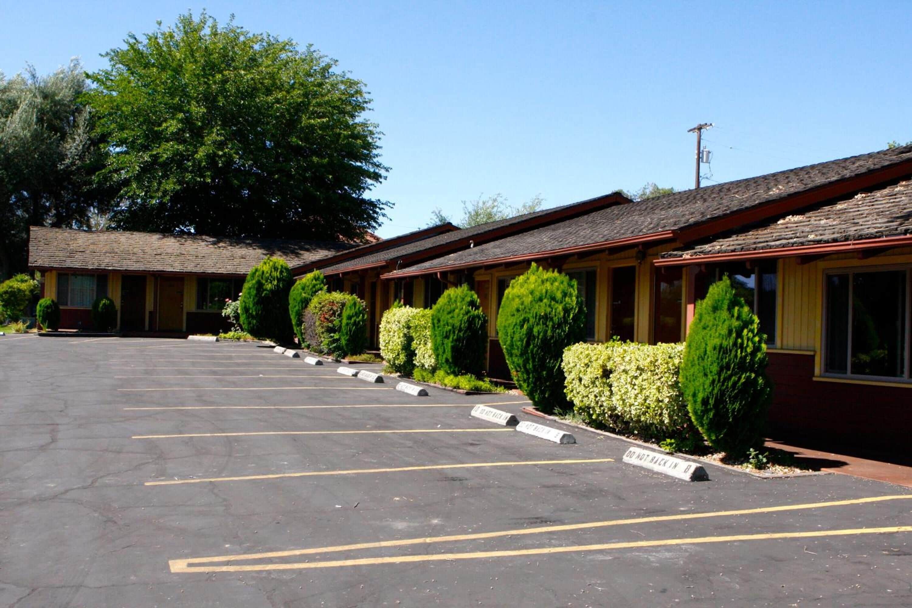 A row of motel rooms with a parking lot in front.