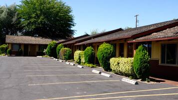 A row of motel rooms with a parking lot in front.
