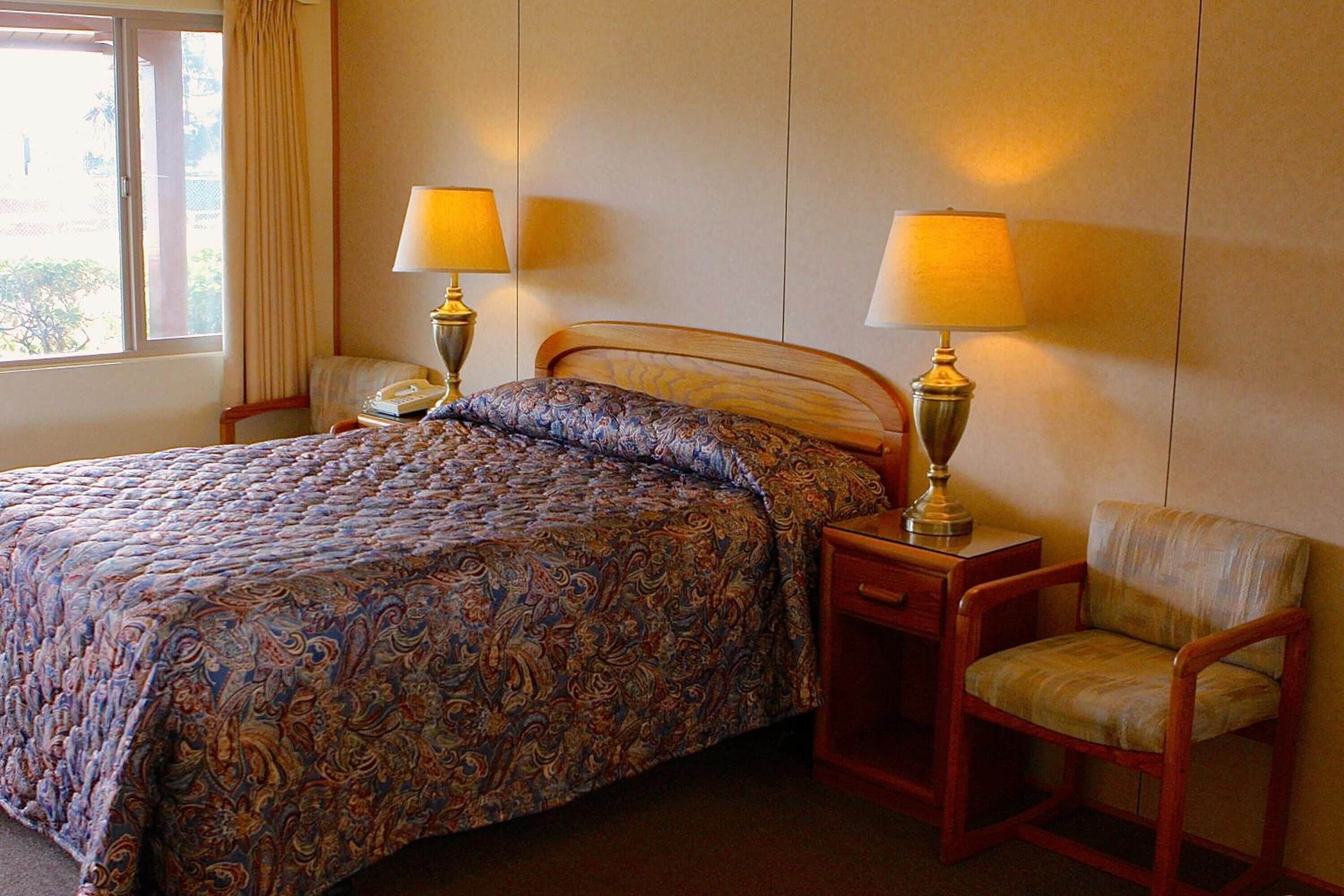 A hotel room with a large bed, two bedside lamps, a chair, and a nightstand.