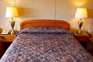 A hotel room with a wooden bed, two bedside lamps, a nightstand with a telephone, and a patterned bedspread.