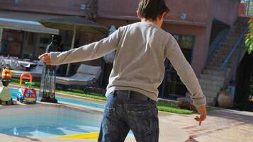 A person skateboarding outdoors near a pool with palm trees and a building in the background.