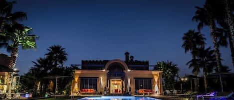 A hotel with a swimming pool, palm trees, and a night sky.