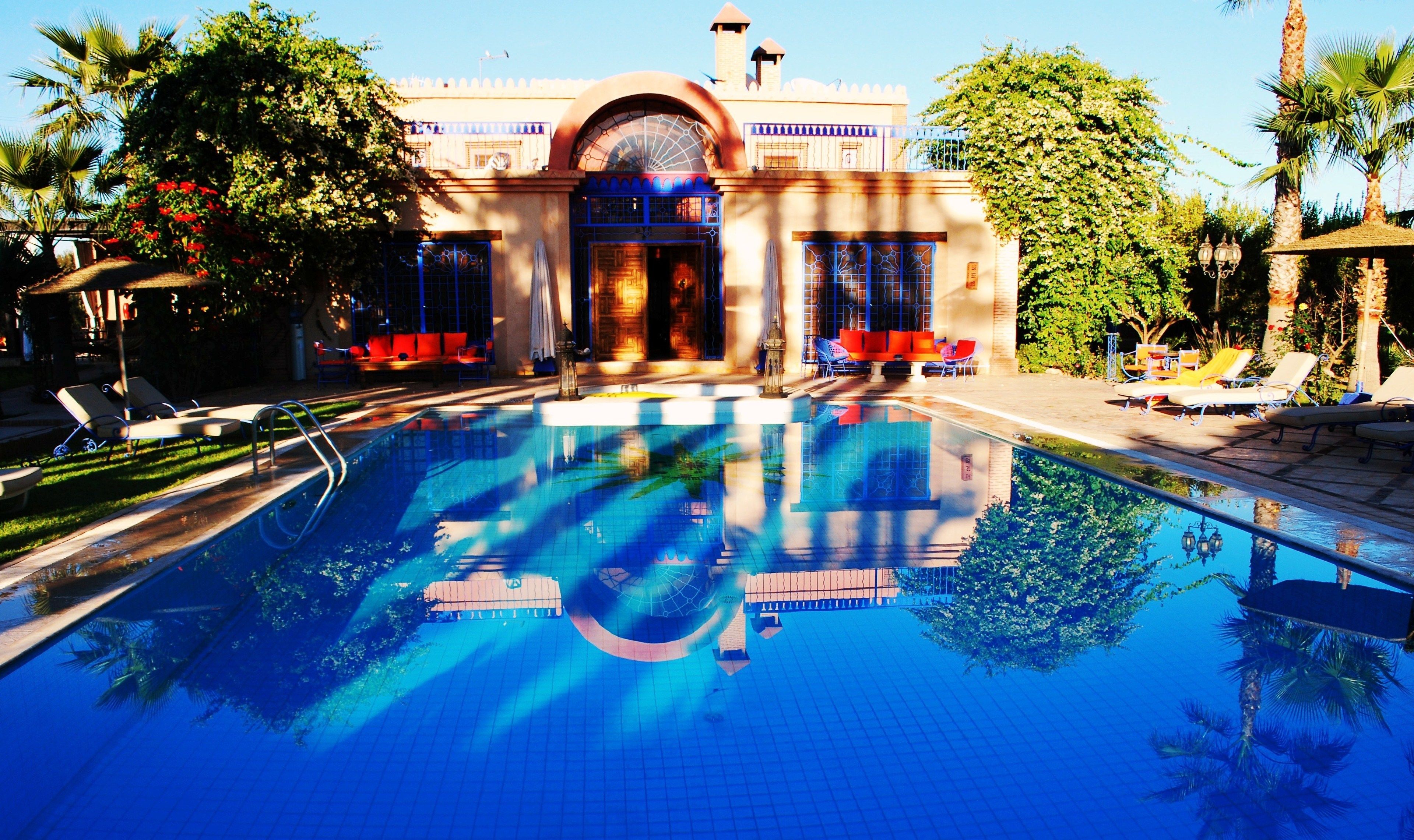 A swimming pool with lounge chairs and a building with arched windows and a dome.