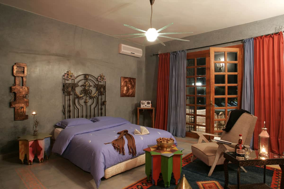 Quarto com cama, cadeira, mesa e janela com cortinas.