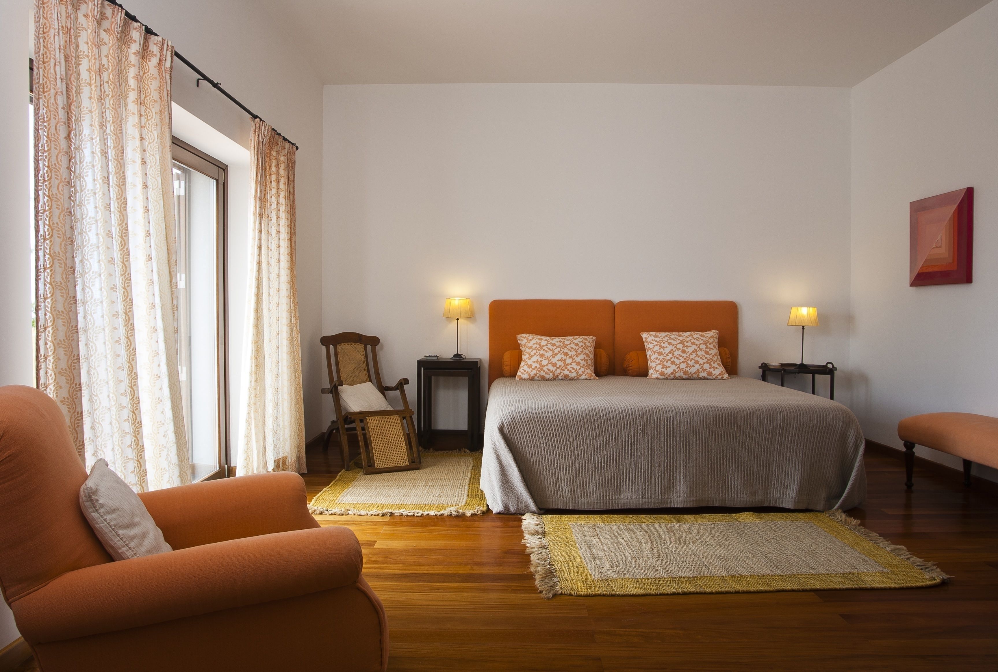 Une chambre à coucher comprenant un lit, deux tables de chevet avec des lampes, une chaise, une petite table et une fenêtre avec des rideaux.