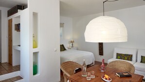 Una habitación con una mesa de comedor de madera, dos sillas de mimbre, un sofá blanco y una lámpara colgante blanca.