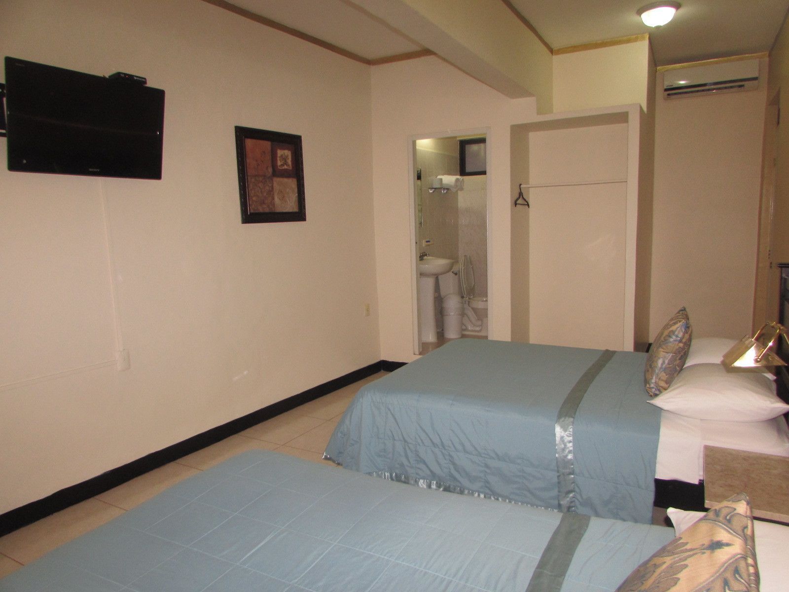 A hotel room with two single beds, a bathroom with a sink and toilet, and a small TV mounted on the wall.