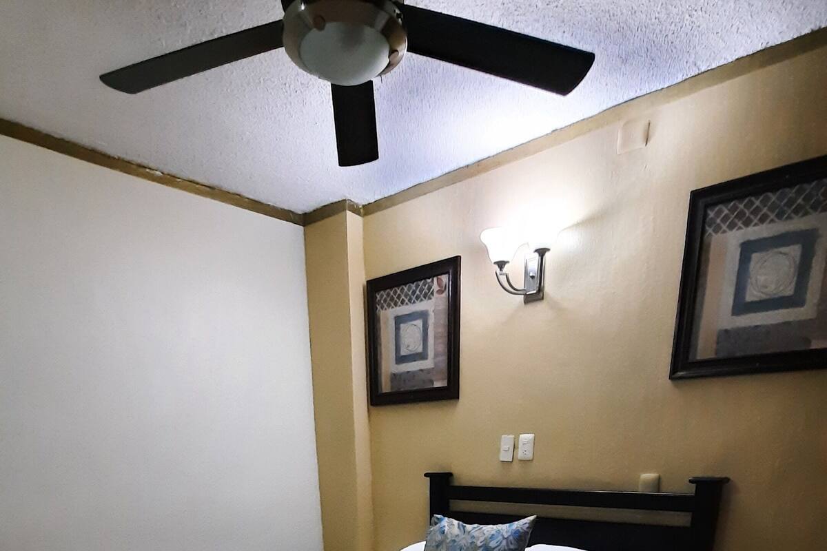 A bedroom with a bed, a nightstand, a ceiling fan, and two wall-mounted light fixtures.