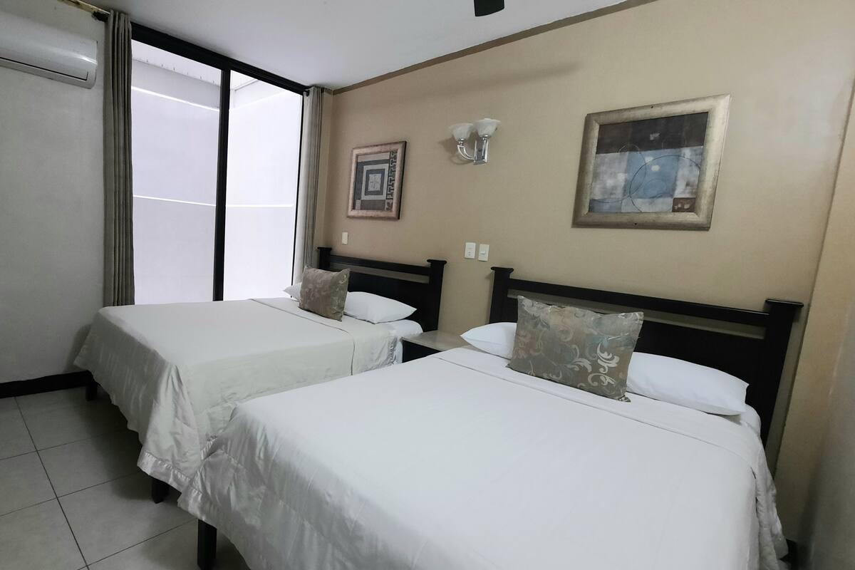 A hotel room with two single beds, a sliding door, a wall-mounted air conditioner, and a framed picture.