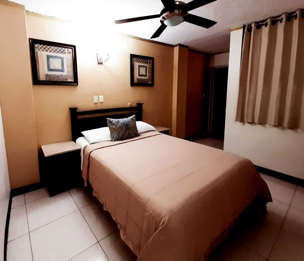 A bedroom with a bed, nightstands, a ceiling fan, and two framed pictures on the wall.