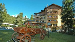 A traditional wooden carriage with flowers parked in front of a multi-story hotel with balconies. - Hotel Bucaneve (Bardonecchia)