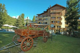 Un carruaje de madera tradicional con flores estacionado frente a un hotel de varios pisos con balcones.