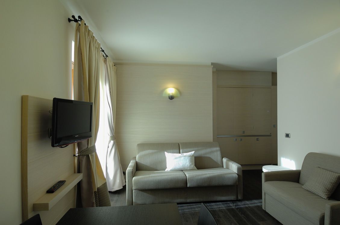 Una camera d'albergo con televisore a schermo piatto montato a parete, un divano, un tavolino e un armadietto.