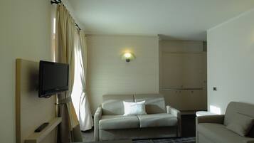 Una camera d'albergo con televisore a schermo piatto montato a parete, un divano, un tavolino e un armadietto.