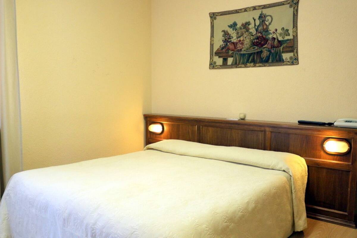 Una cama bien hecha con cabecera de madera y lámparas de noche, un cuadro floral enmarcado en la pared y una pared lisa.