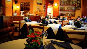 A restaurant with multiple tables set for dining, featuring a warm interior with wooden furniture and decorative wall shelves. - Hotel Bucaneve (Bardonecchia)