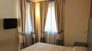 A hotel room with a bed, curtains, a television mounted on the wall, and a bedside table. - Hotel Bucaneve (Bardonecchia)