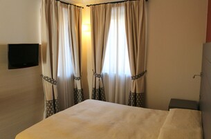 Una habitación de hotel con cama, cortinas, un televisor montado en la pared y una mesita de noche.