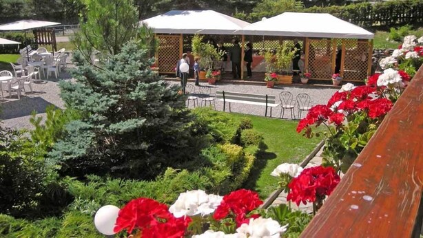 An outdoor seating area with white tables and chairs, surrounded by potted plants and flowers. - Hotel Bucaneve (Bardonecchia)