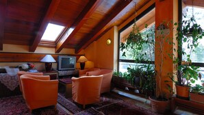 A cozy living room with wooden beams, a television, orange chairs, and potted plants. - Hotel Bucaneve (Bardonecchia)