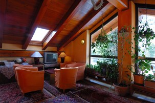 Una sala de estar acogedora con vigas de madera, un televisor, sillones naranjas y plantas en macetas.