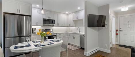 A modern kitchen with white cabinets, stainless steel appliances, and a dining area with a table set for four.