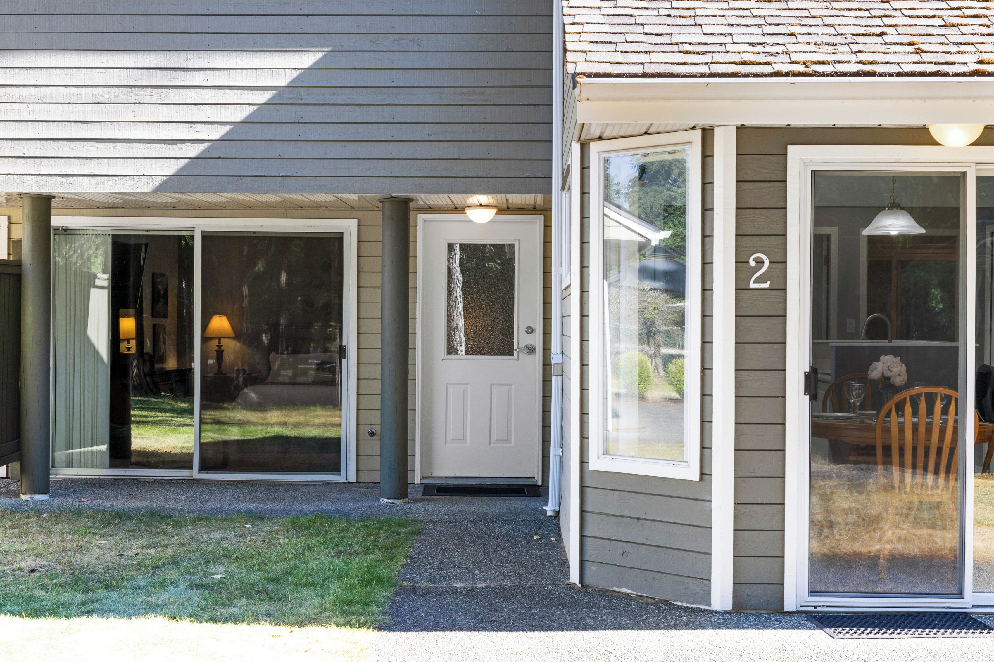 A house with a sliding glass door entrance, a number '2' on the door, and a visible outdoor seating area with a table and chairs.
