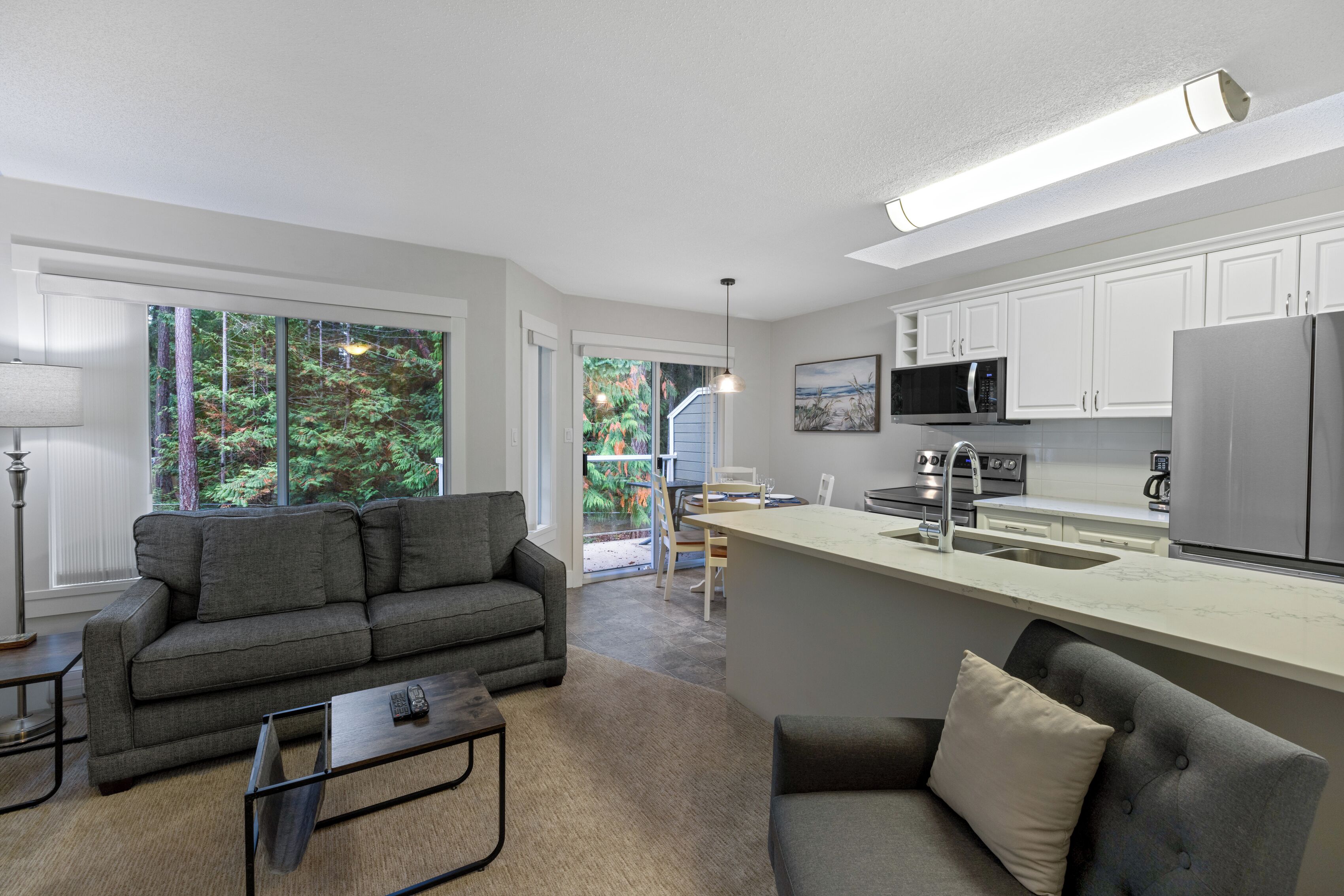 A modern kitchen with white cabinets, a stainless steel refrigerator, and a dining area with a table and chairs.