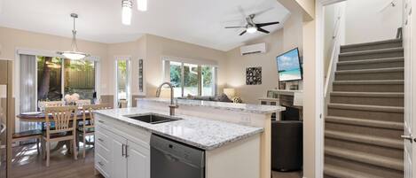 A modern kitchen with a central island, built-in dishwasher, and a dining area with wooden chairs.