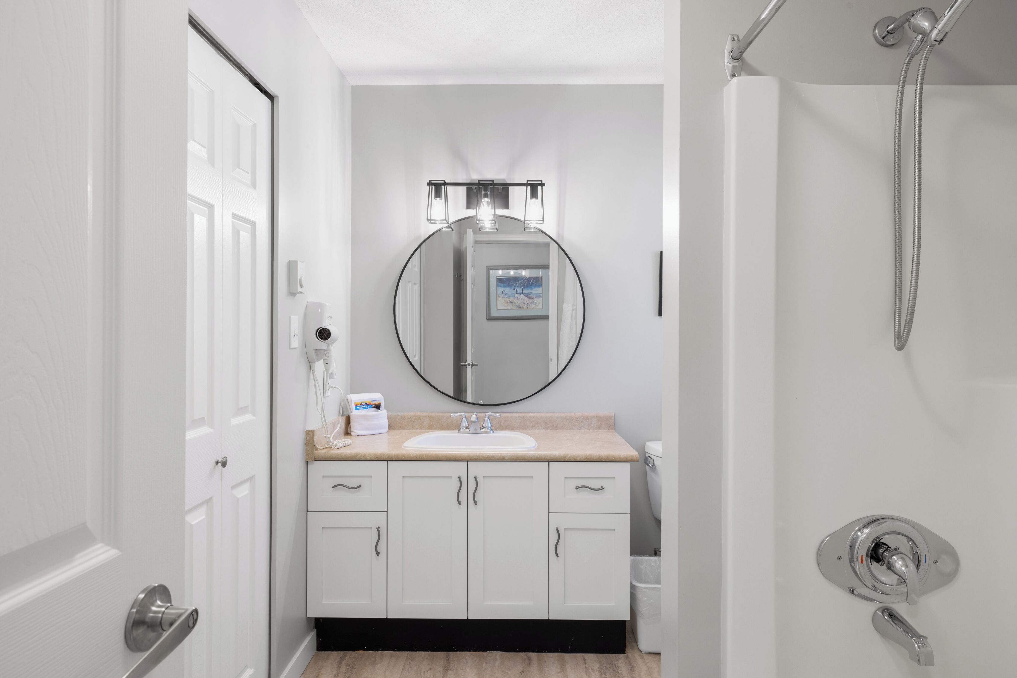 A modern bathroom with a white sink, a round mirror, and a shower.