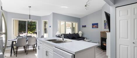 A modern kitchen with a central island, a dining area with chairs, and a sofa.