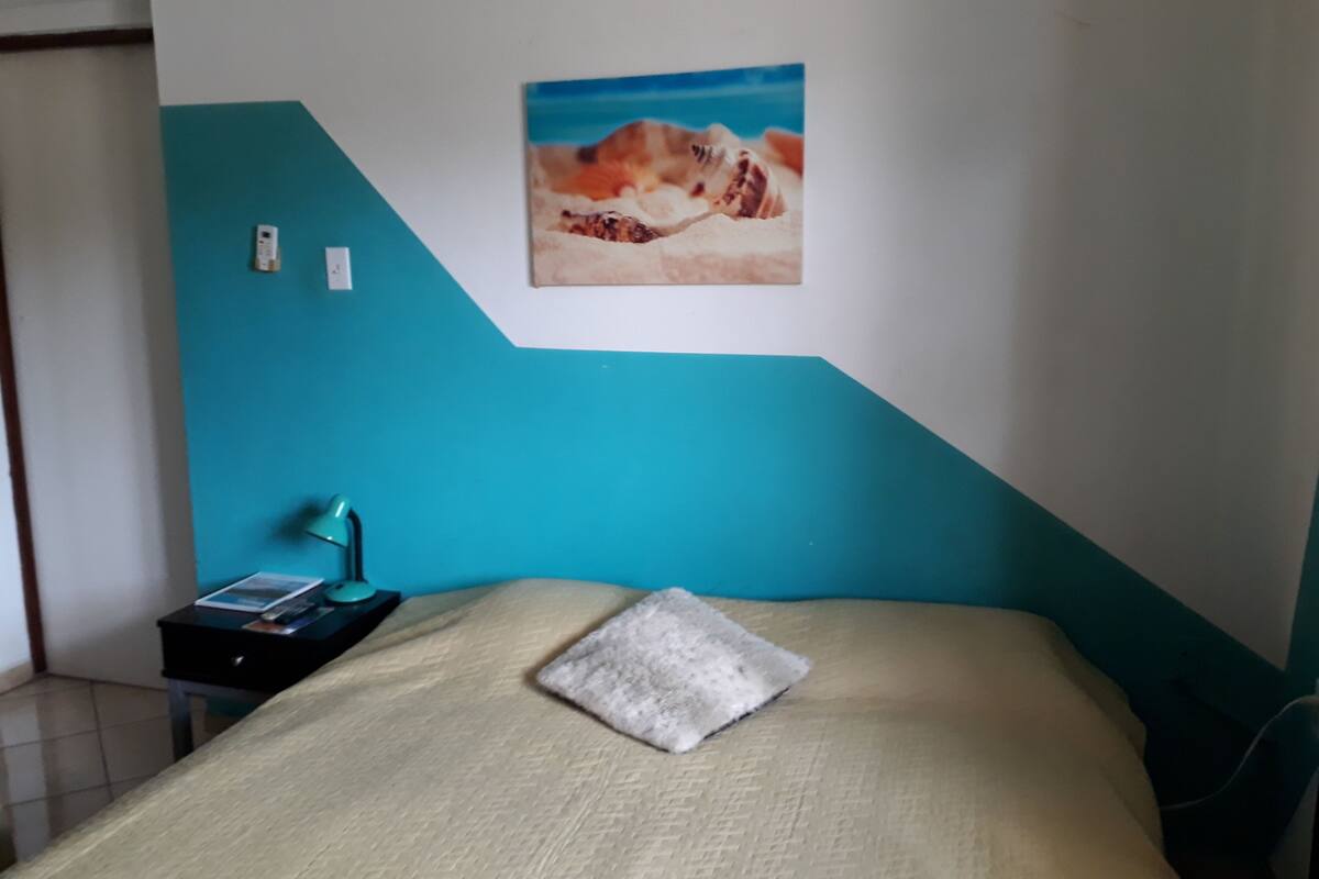 A bedroom with a bed, a nightstand, a lamp, and a painting on the wall.