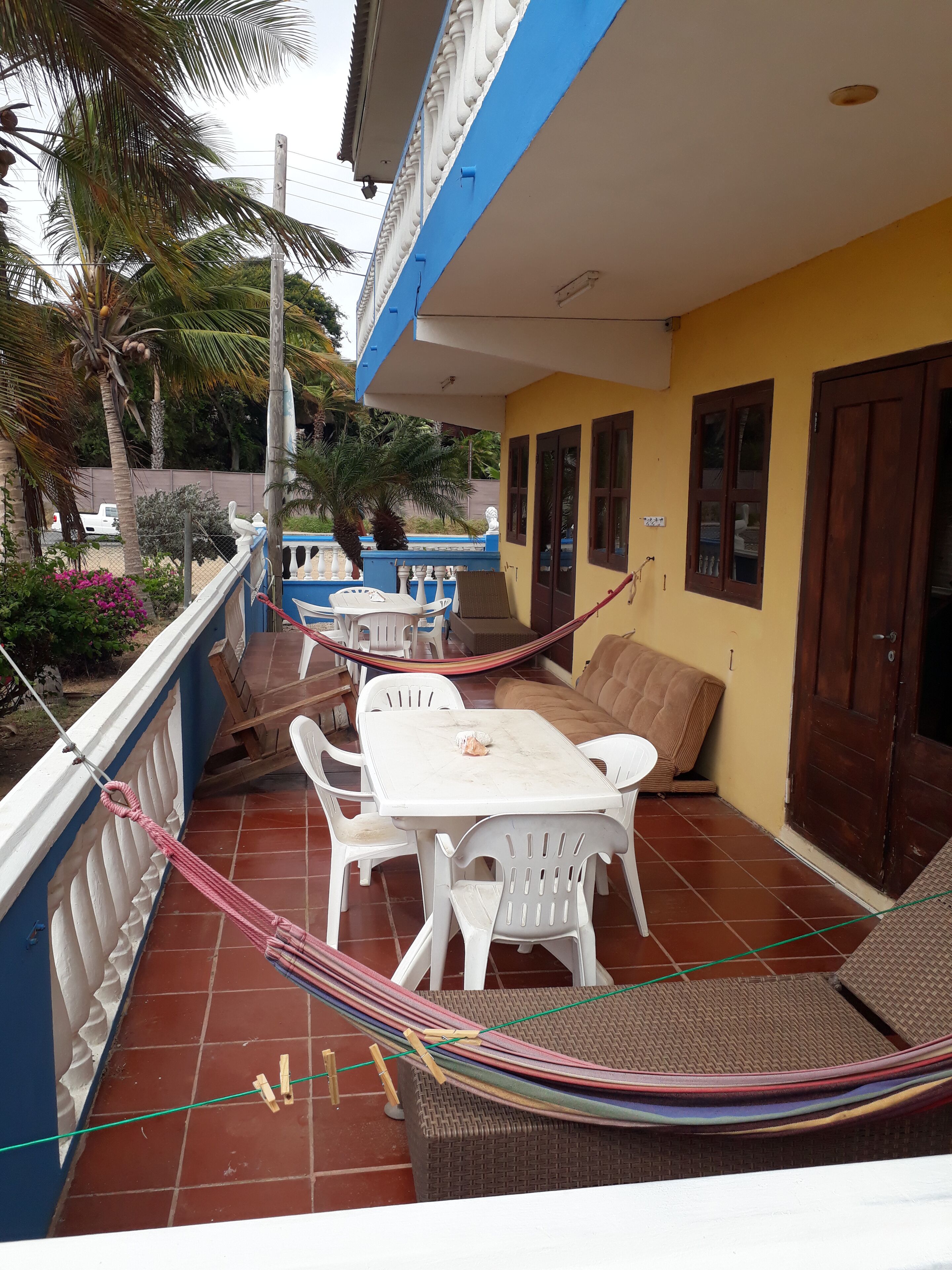 Une terrasse avec une table et des chaises blanches, un hamac et un canapé marron.