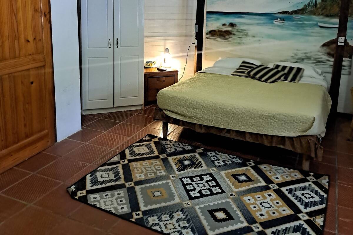 A bedroom with a bed, a nightstand, a wardrobe, and a beach-themed wall mural.