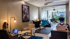 Een moderne lounge met comfortabele zithoeken, een laptop op een tafel en een groot kunstwerk in een lijst aan de muur.
