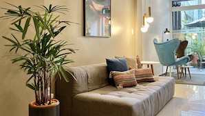 Een moderne woonkamer met een bank, een grote potplant en een lijst met kunstwerk aan de muur.