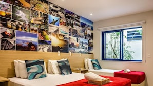Een hotelkamer met een grote wand waarop foto’s van verschillende bestemmingen staan, een bed met rode beddengoed, een klein tafeltje en een raam met uitzicht op bamboe.