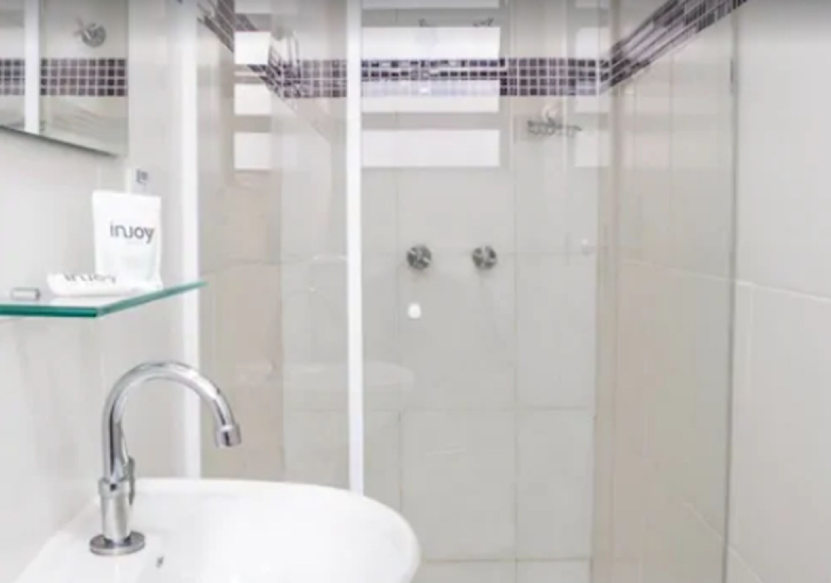 Une salle de bain moderne avec une douche à parois de verre, un lavabo blanc et une étagère en verre sur laquelle est posée une serviette.