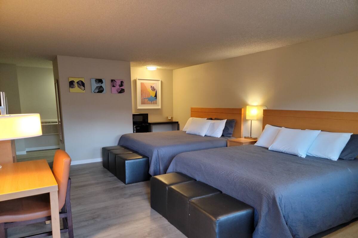 Une chambre d’hôtel avec deux lits, un bureau, une chaise et une petite kitchenette.